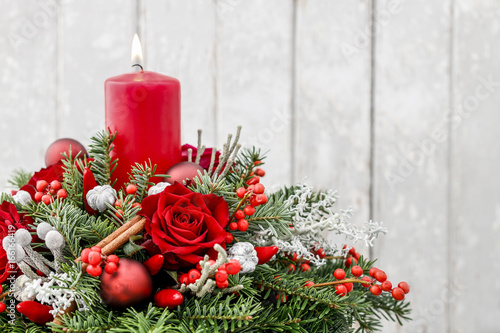 Christmas decoration with candle, red roses, fir, brunia and cinnamon sticks.