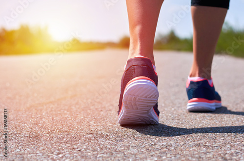 young girl in running shoes runs along road, only her legs are visible, legs and sneakers, sunlight