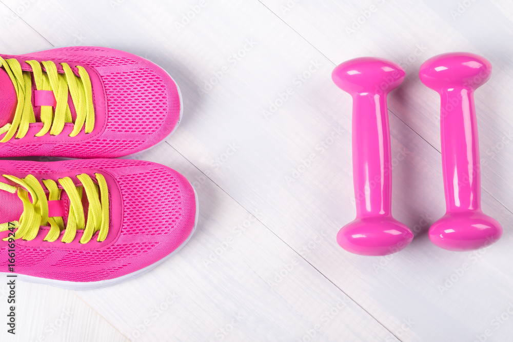 Pink set of dumbbells and sneakers on a wooden gray background Pink set of dumbbells and sneakers on a wooden gray background