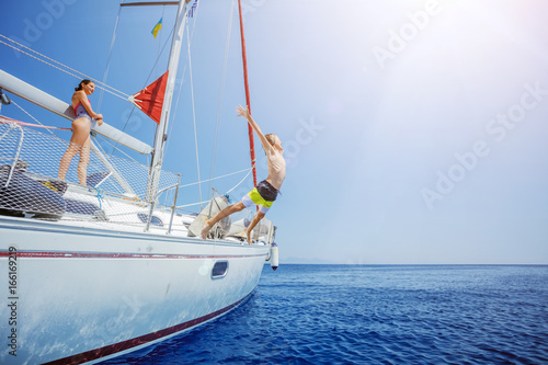 Boy with his sister jump of sailing yacht on summer cruise. Travel adventure, yachting with child