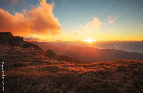 Red and orange sunset in the mountains in autumn time. Landscape with sunny beams. Dramatic scene. In the background view of the sea