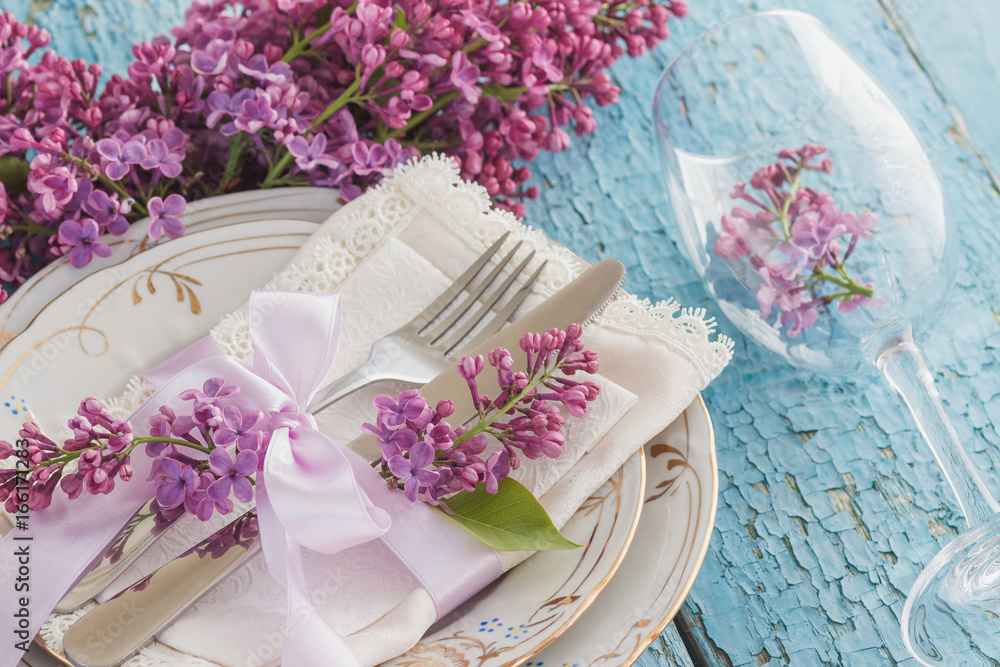 Tableware and silverware with bunches of violet lilac on the wooden background Tableware and silverware with bunches of violet lilac on the wooden background