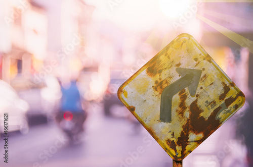 Old curve road warning sign on blur traffic road with colorful bokeh light abstract background.
