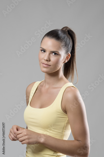 Beautiful young sporty woman with high ponytail hair looking at camera over gray studio background.