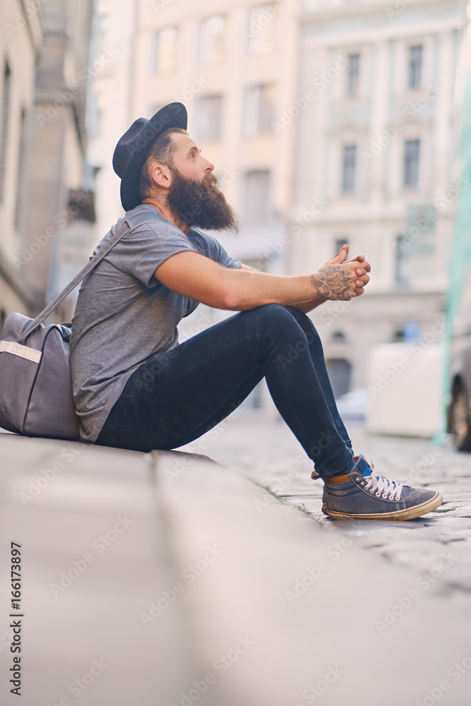 Casual bearded hipster sits on a step on a street.
