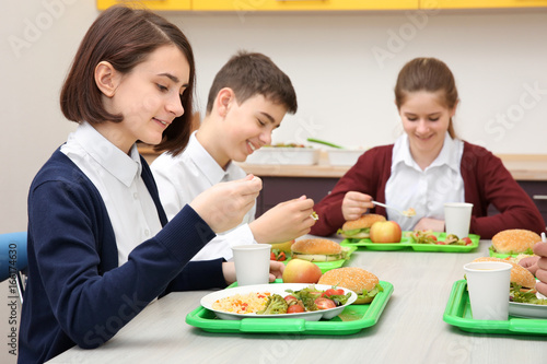 Children sitting at table in school cafeteria while eating lunch photo