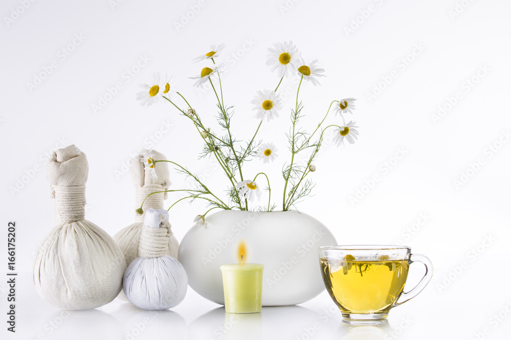 Bouquet of chamomiles flowers in a white vase and a transparent cup with tea on a white background. Herbal balls, spa.