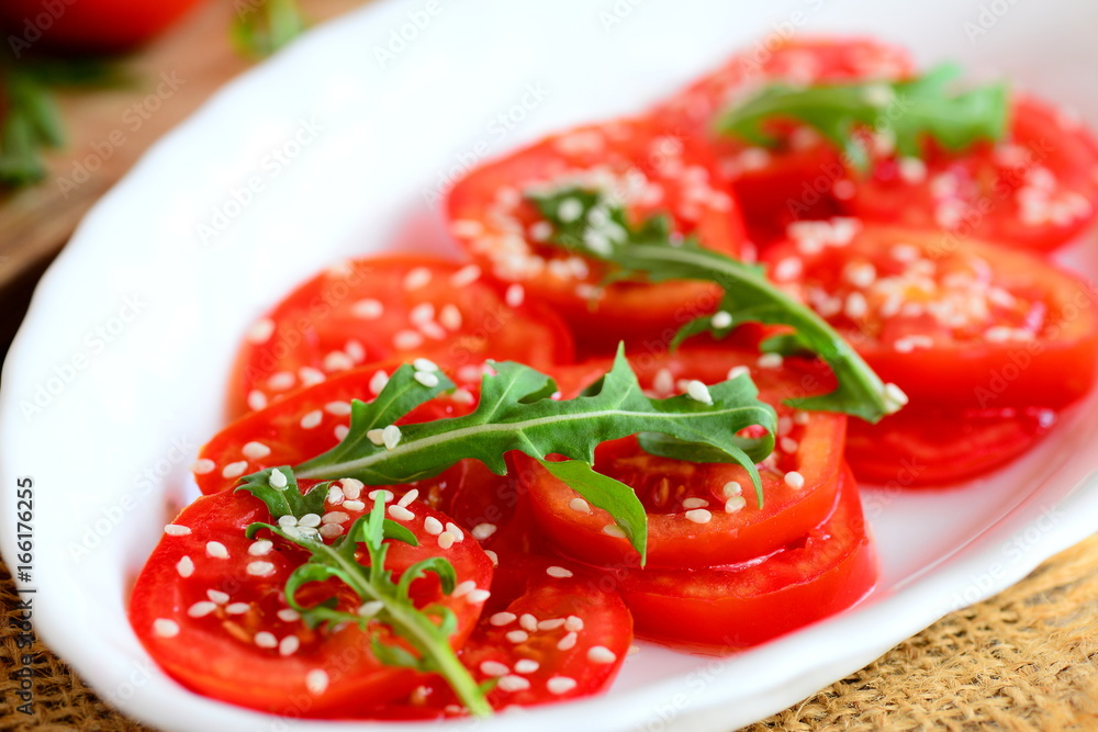 Fresh tomato slices, arugula rocket and sesame seeds salad. Low calorie salad on a white plate and burlap napkin. Diet lunch or dinner idea. Closeup Fresh tomato slices, arugula rocket and sesame seeds salad. Low calorie salad on a white plate and burlap napkin. Diet lunch or dinner idea. Closeup