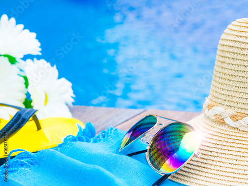 Sunglasses with summer hat, flip flops   and flowers by the swimming pool. Vacation and relaxation, summer travel concept.