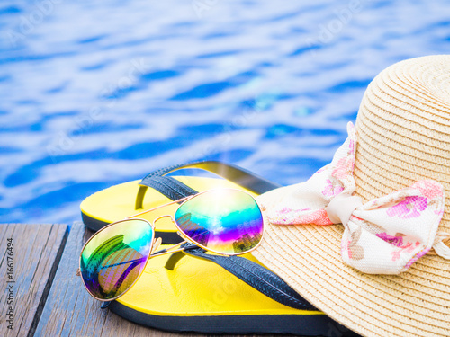 Summer hat with  sunglasses and flip flops by the swimming pool. Vacation and relaxation, summer travel concept.