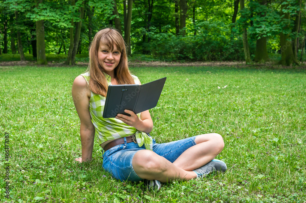 Woman with tablet sitting on grass in park Woman with tablet sitting on grass in park