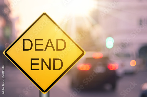 Dead end warning sign on blur traffic road with colorful bokeh light abstract background.