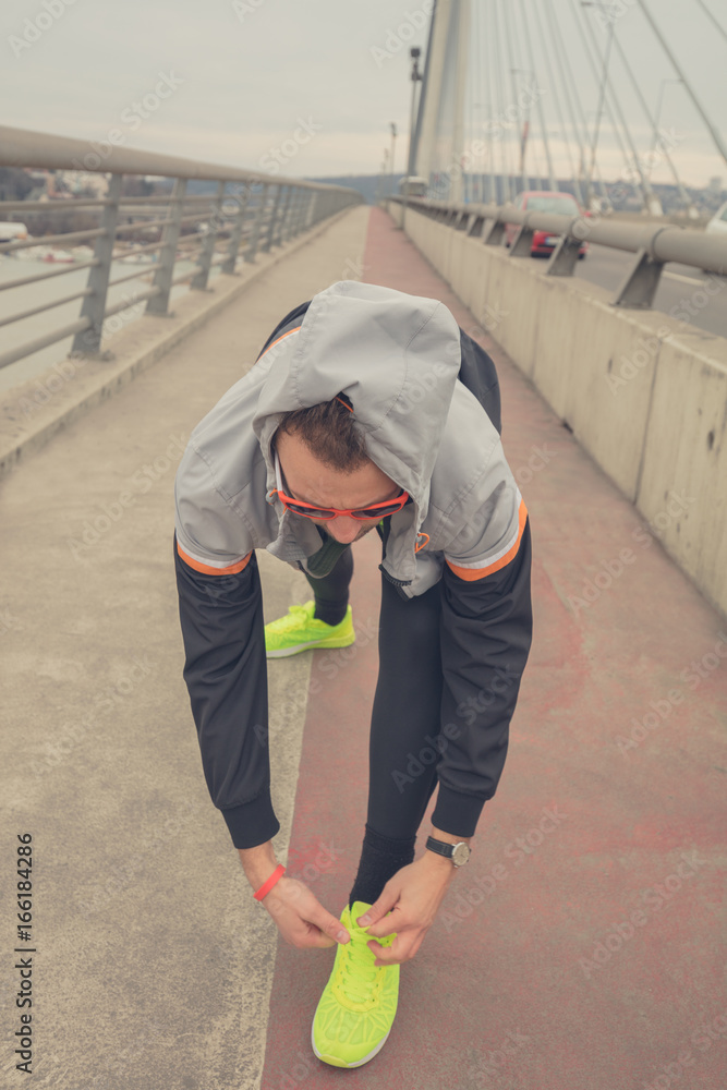 Man tying running shoes on a big bridge.