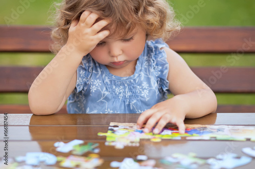 Photo Difficult task. Tired child playing jigsaw with serious face.