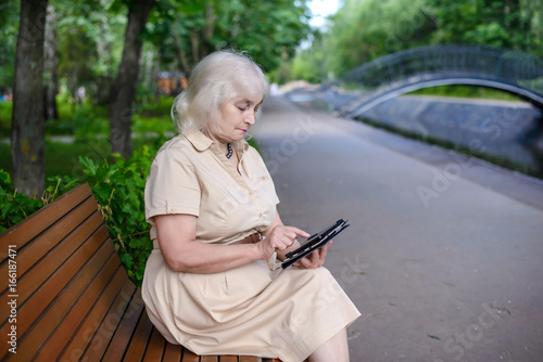 An elderly woman with tablet computer in the park
