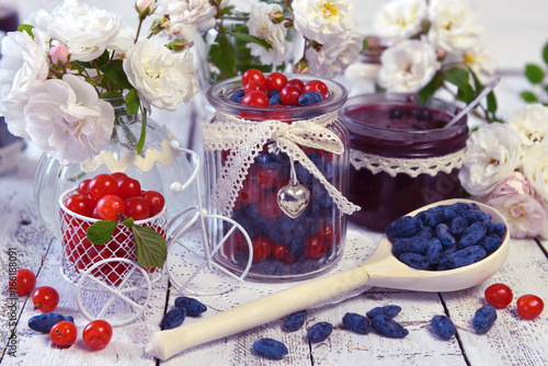Wooden spoon full of honey berry, vintage jars with fresh berry and jam against the background with roses.