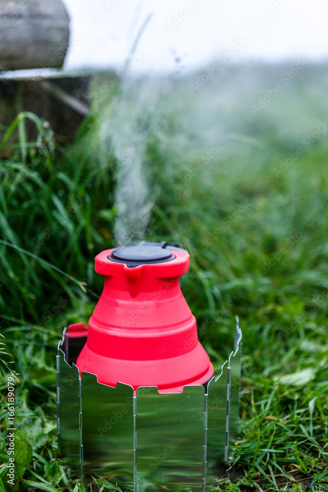 Fodable camping kettle with boiling water standing on burning stove. Fodable camping kettle with boiling water standing on burning stove.