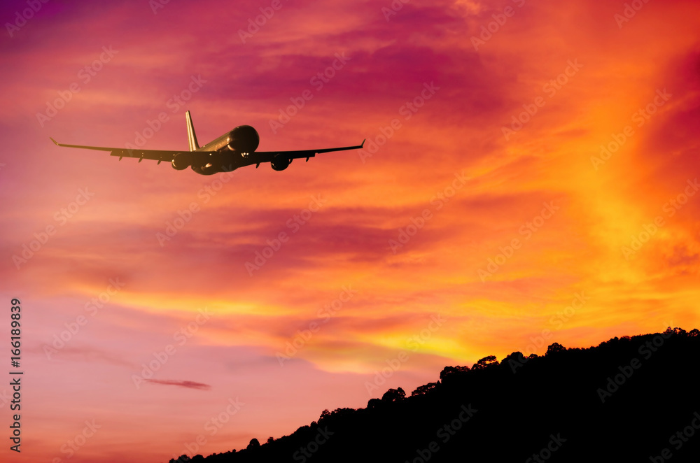 Obraz premium Airplane flying over mountain and sunset sky background.