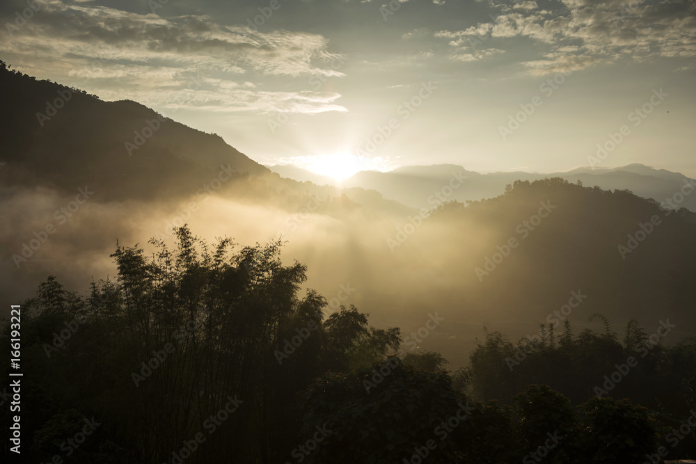 Obraz premium Morning sun rays through the fog over mountain slopes.