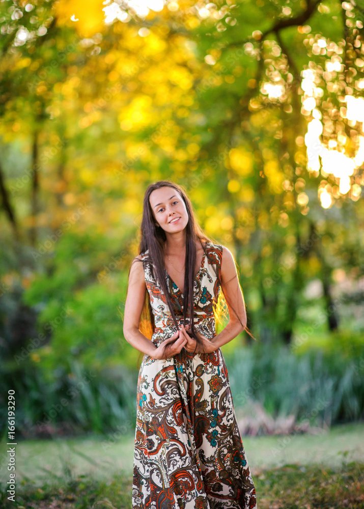 young girl with long hair and in a beautiful dress walks and has fun outdoors on a sunset
