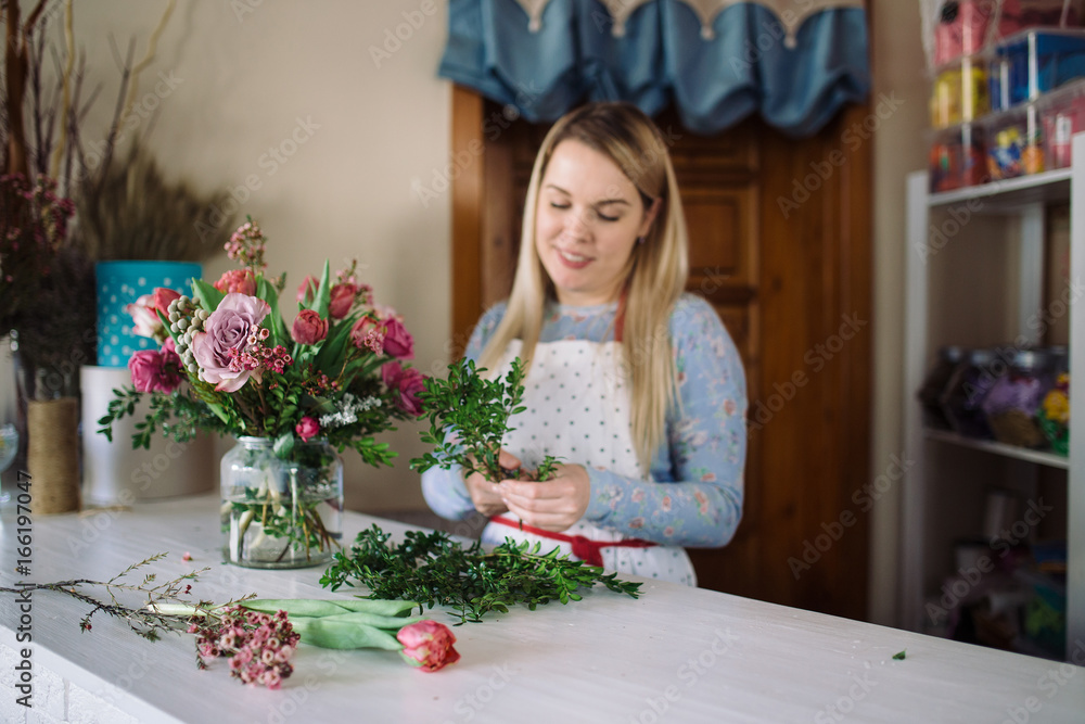 woman florist making bouquet of flowers indoor. Female florist preparing bouquet with roses, tulip in flower shop