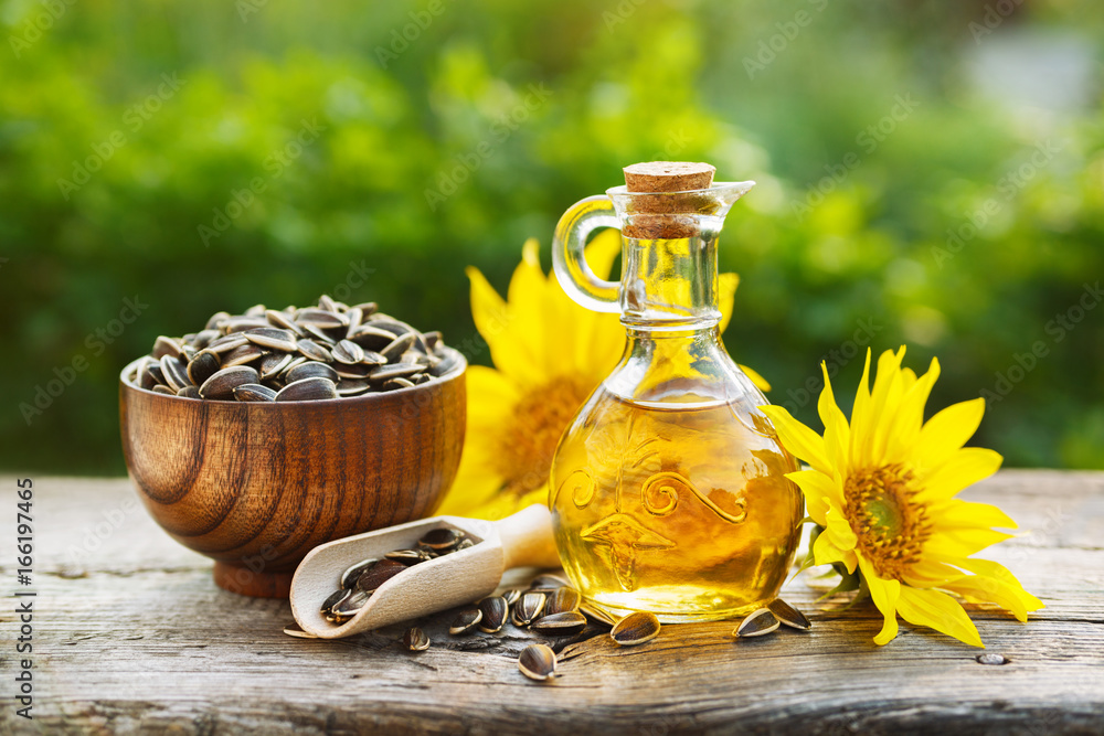 Organic sunflower oil in a small glass jar with sunflower seeds and fresh flowers. Outdoors - obrazy, fototapety, plakaty 