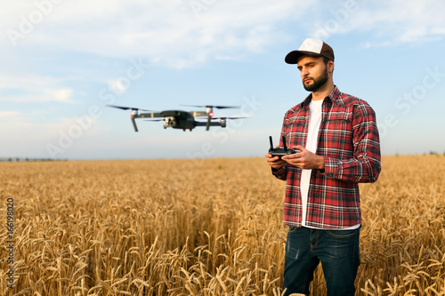 Compact drone hovers in front of farmer with remote controller in his hands. Quadcopter flies near pilot. Agronomist taking aerial photos and videos in a wheat field