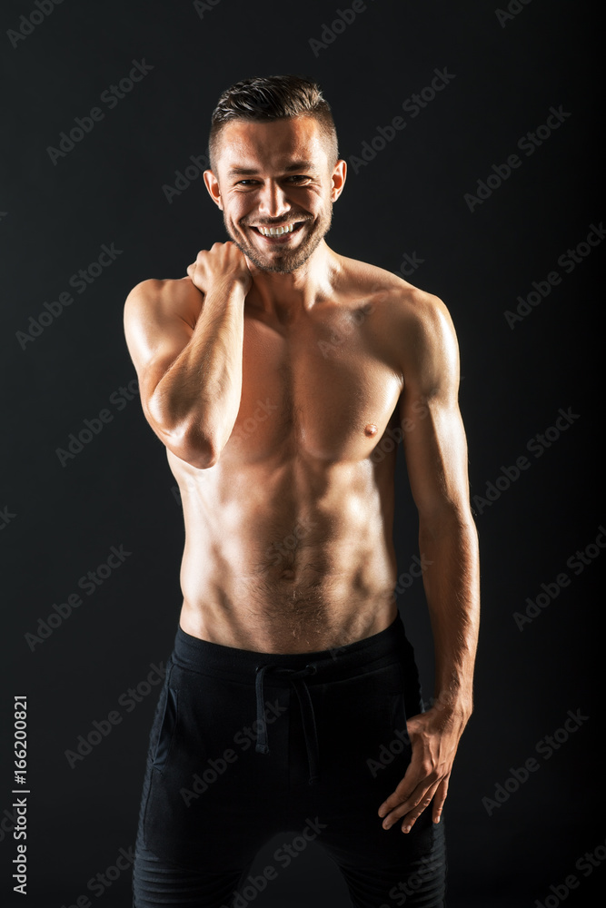 Smiling muscular shirtless man against dark background