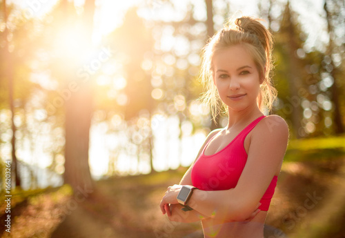 Attractive fit athletic woman in a forest, wearing smart watch, taking a break from intense workout. Sport, fitness, workout concept