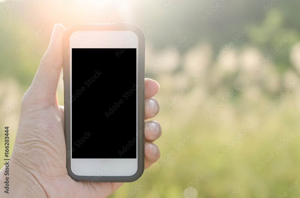 Copy space hand using smart phone and sun light in nature green park background. Travel adventure lifestyle and business economic concept.