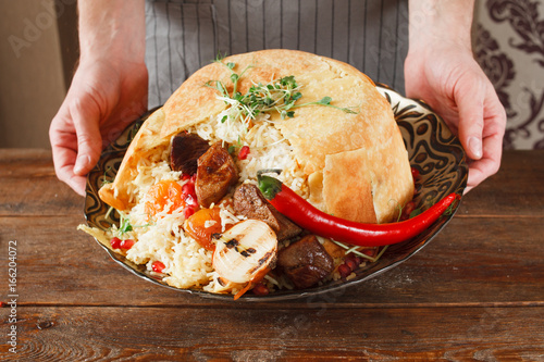 Shah pilaff on big plate holding in hands. National georgian cuisine, spicy rice with meat under lavash decorated chili pepper photo