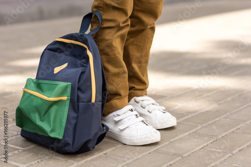 cropped shot of stylish schoolboy standing with backpack on street photo
