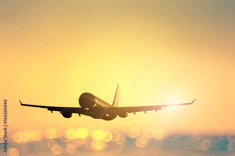 Airplane flying over blur tropical beach with smooth wave and sunset sky abstract background.