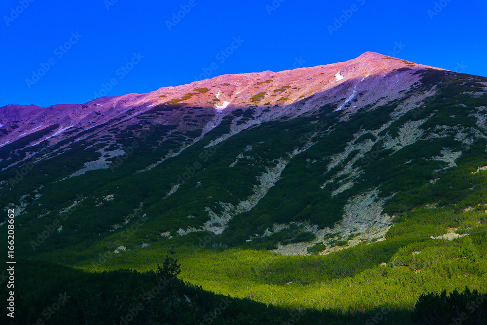 Beautiful view on the high green mountains peaks, on the colorful sunrise sky background. Mountain hiking paradise landscape, no people.