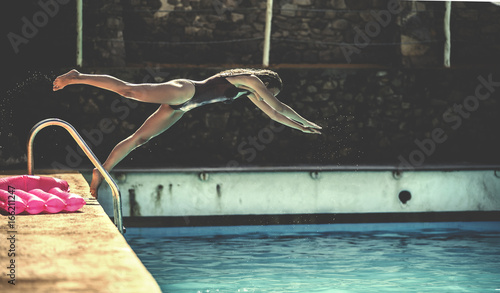 A young woman wearing a swimsuit diving into a swimming pool.