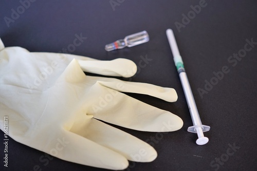 White glove, syringe and glass ampoule on black background