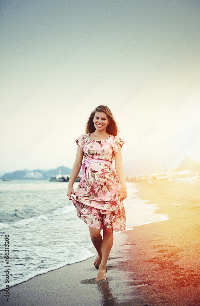 Pretty smiling pregnant female walking on the beach. Concept of health care and maternity. 