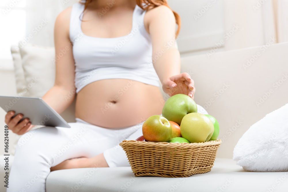 cropped view of pregnant woman with digital tablet eating apples at home cropped view of pregnant woman with digital tablet eating apples at home