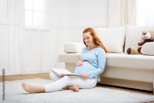 attractive redhead pregnant woman reading book at home