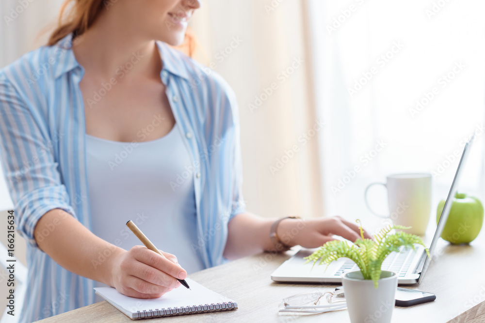 cropped view of pregnant woman using laptop and writing in notepad at home cropped view of pregnant woman using laptop and writing in notepad at home