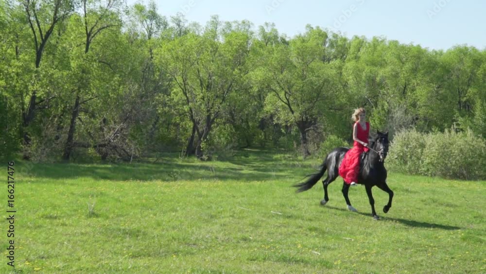 Young woman in red dress riding black horse bareback. Young woman in red dress riding black horse bareback.