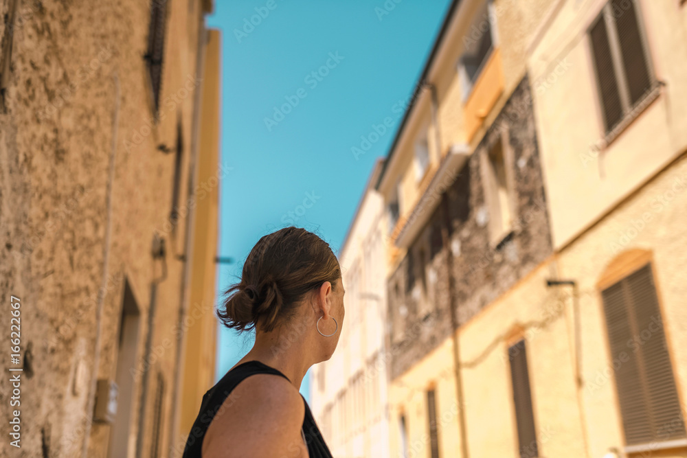 Rear view of brunette woman looking in street of old italian town. Sardinia. Italy.
