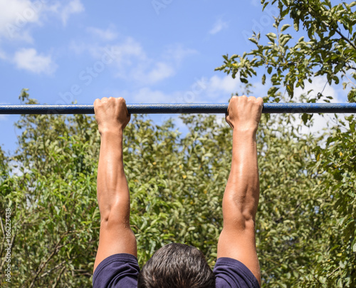 Hands on the bar close-up. The man pulls himself up on the bar. Playing sports in the fresh air. Horizontal bar.