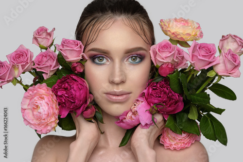 Studio portrait of a beautiful young woman. Fashion brunette Model with perfect makeup, nude lips and clean fresh skin. Flowers near the face 