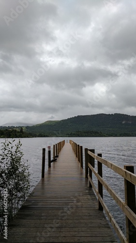 Fototapeta Naklejka Na Ścianę i Meble -  Wood pier leading to a cold lake with mountains in the background