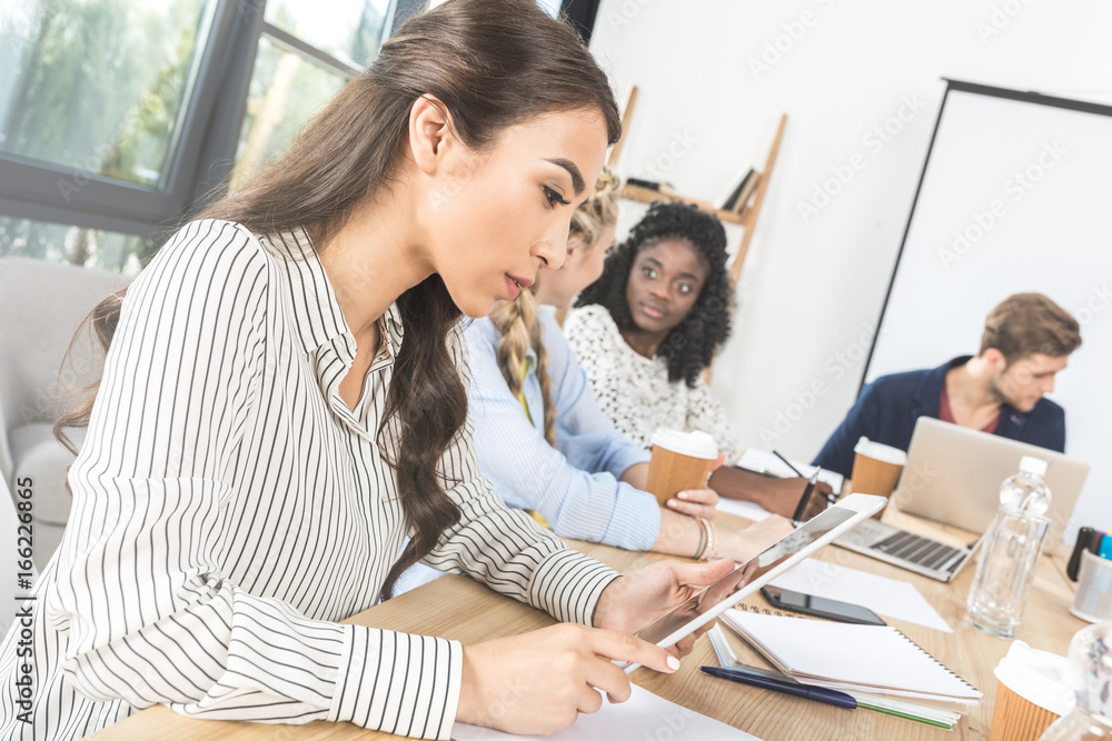 side view of focused asian businesswoman using tablet during meeting with colleagues in office side view of focused asian businesswoman using tablet during meeting with colleagues in office