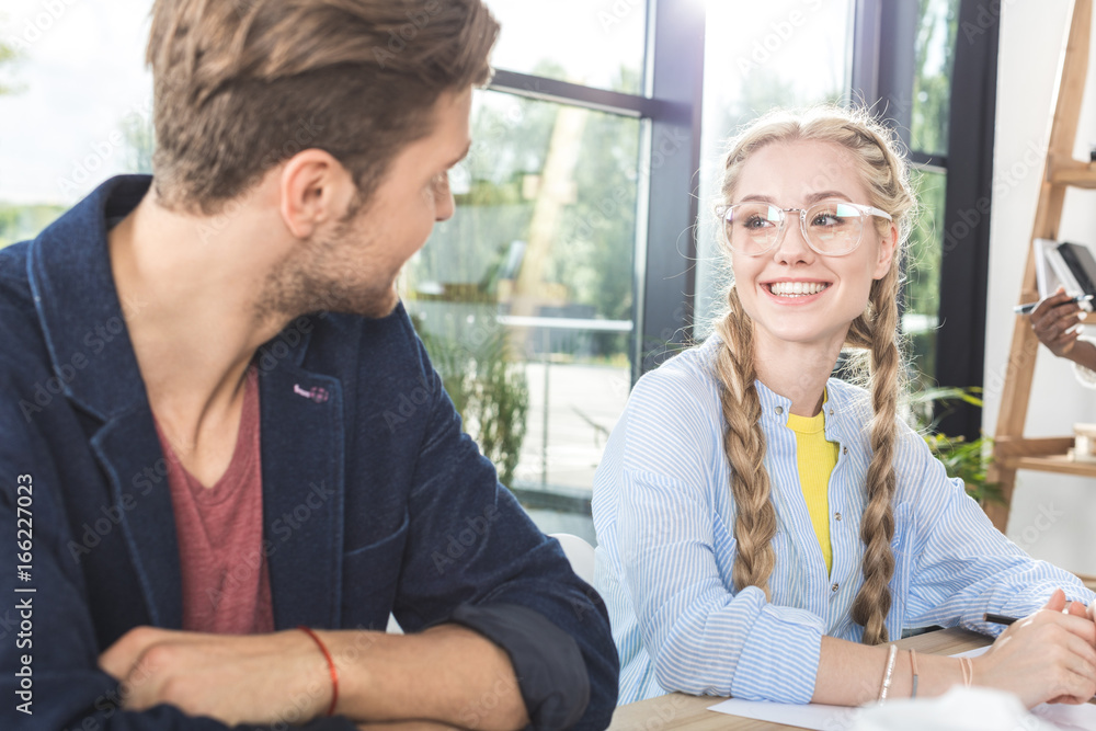 portrait of smiling business colleagues having conversation while sitting at table in office portrait of smiling business colleagues having conversation while sitting at table in office
