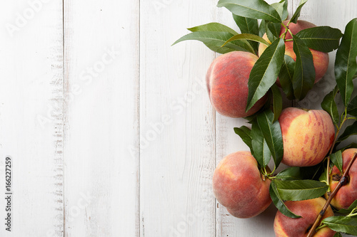 Fresh peaches fruits with leaves on wooden background, top view