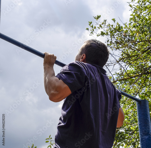 The man pulls himself up on the bar. Playing sports in the fresh air. Horizontal bar.