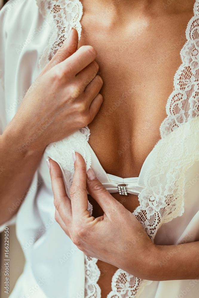 Close-up image of the sexual bride in silk lingerie. Hands on the bride's breast in a white robe.